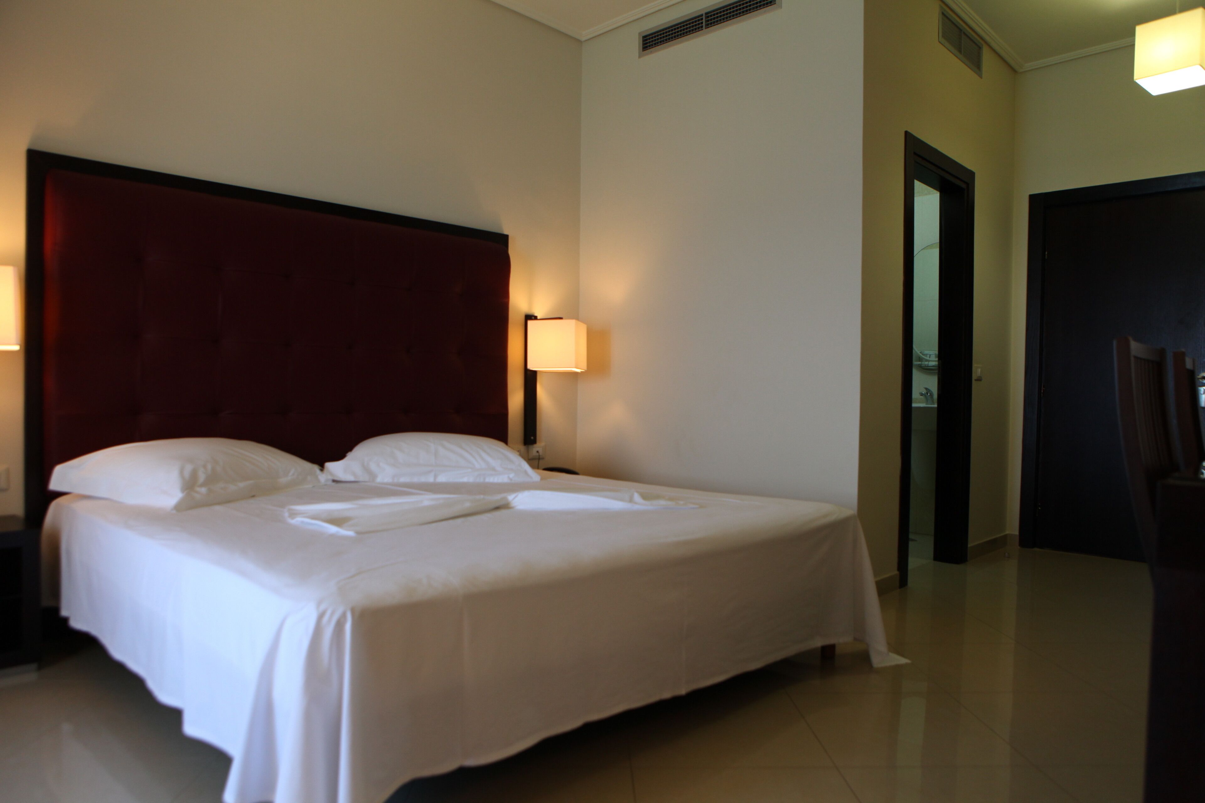 A neatly made bed with white linens and a red headboard in a hotel room.
