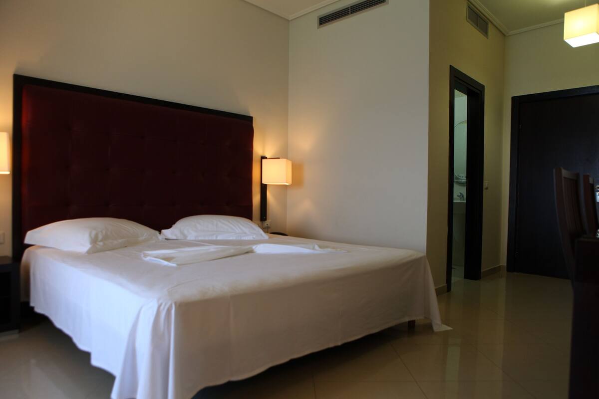 Una cama bien hecha con sábanas blancas y un cabecero rojo en una habitación de hotel.