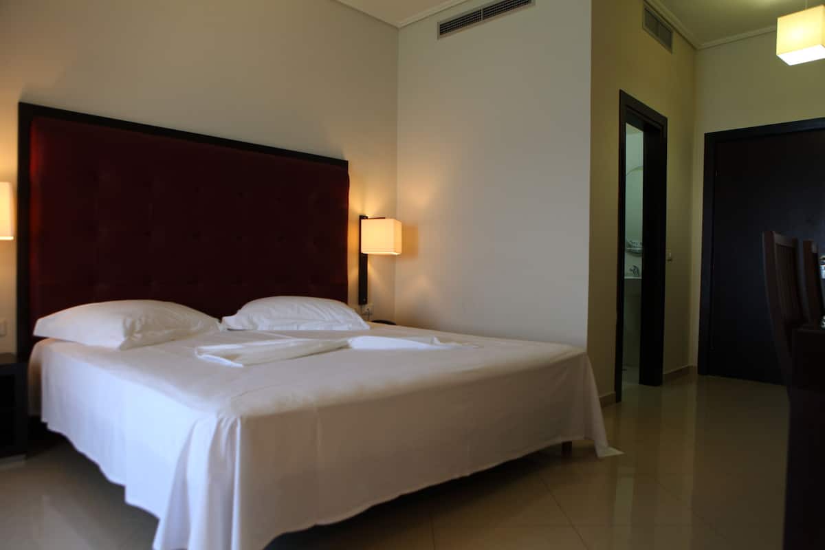 A neatly made bed with white linens and a red headboard in a hotel room.