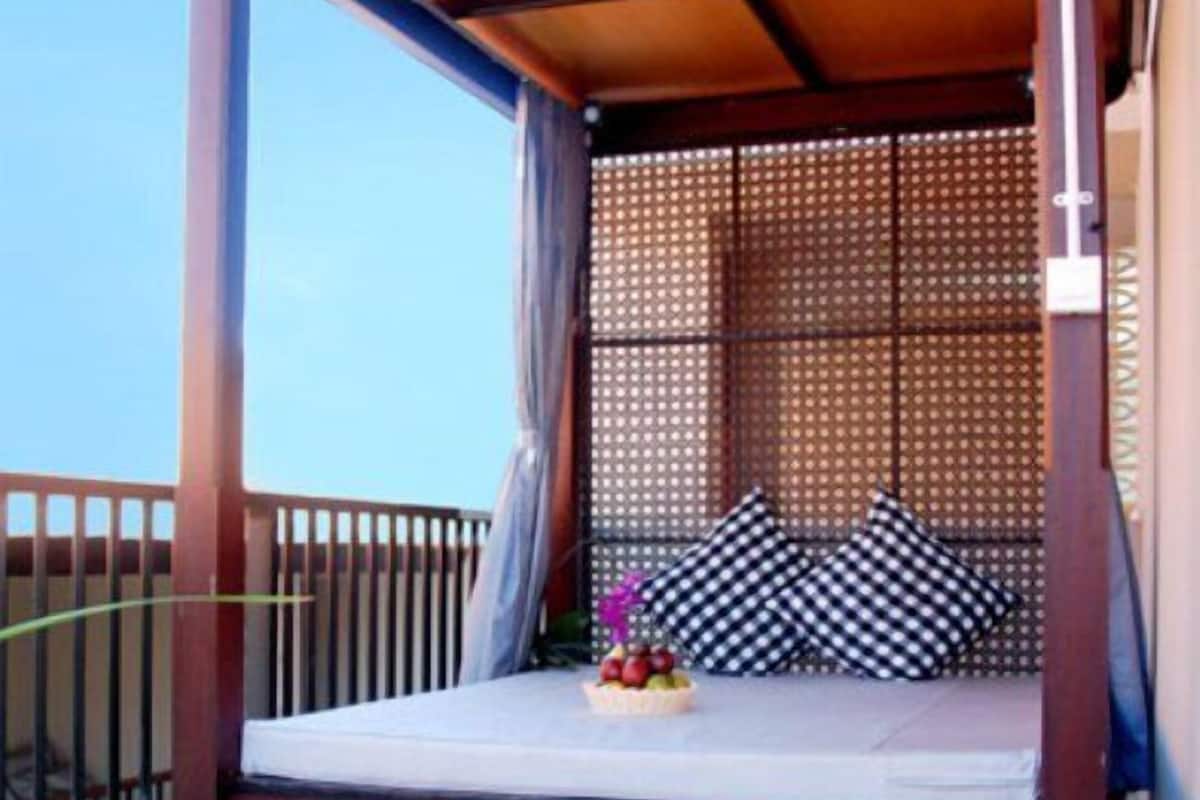 A wooden bed with a canopy, a small table with flowers, and a patterned cushion on a balcony.