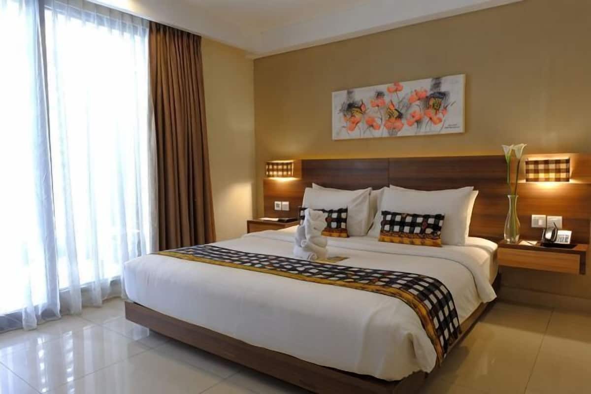 A hotel room with a large bed, two bedside tables, a nightstand, a painting on the wall, and a window with curtains.