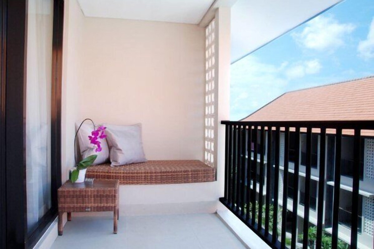 A balcony with a wicker bench, a small table with a plant, and a view of the building's exterior.