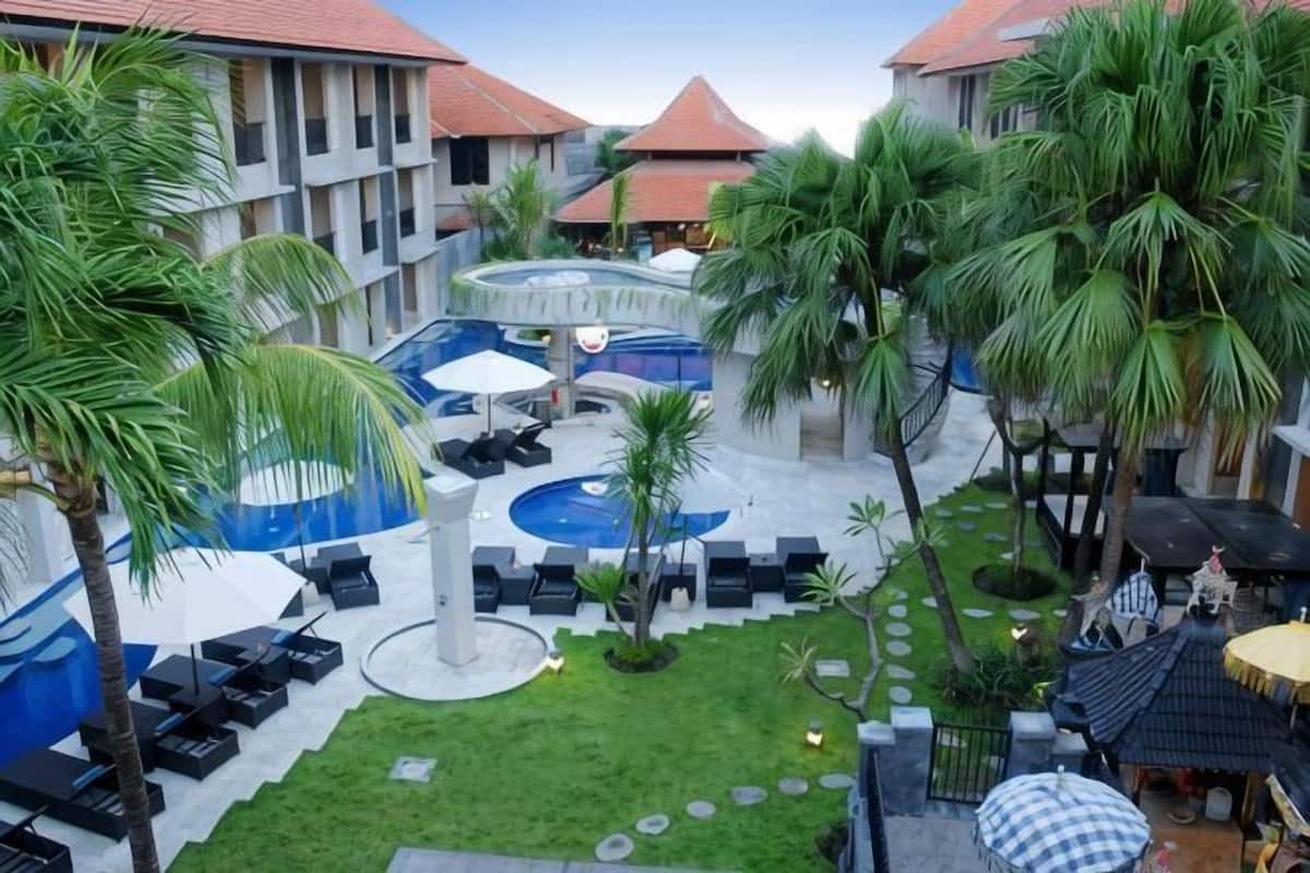 A courtyard with a pool, lounge chairs, palm trees, and a small garden area.