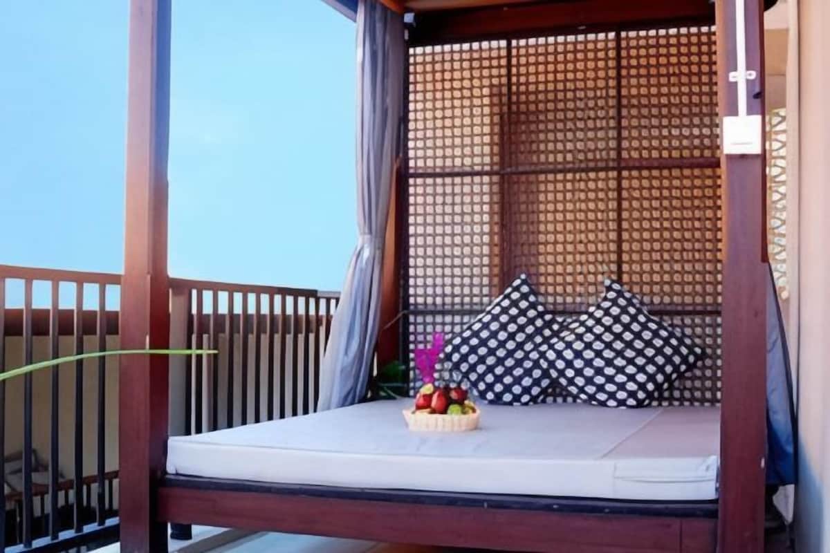 Un balcón con una cama de madera, cojines estampados y un frutero.