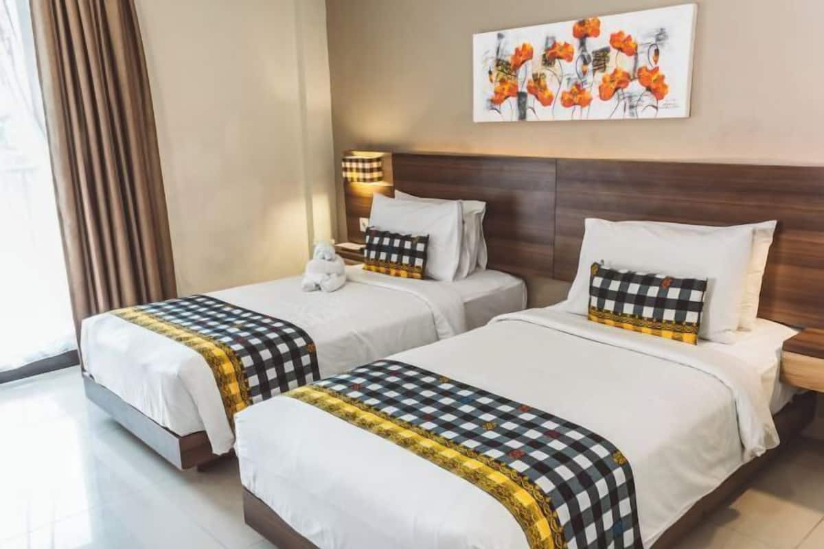 A hotel room with two beds, a nightstand, a lamp, and a painting on the wall.
