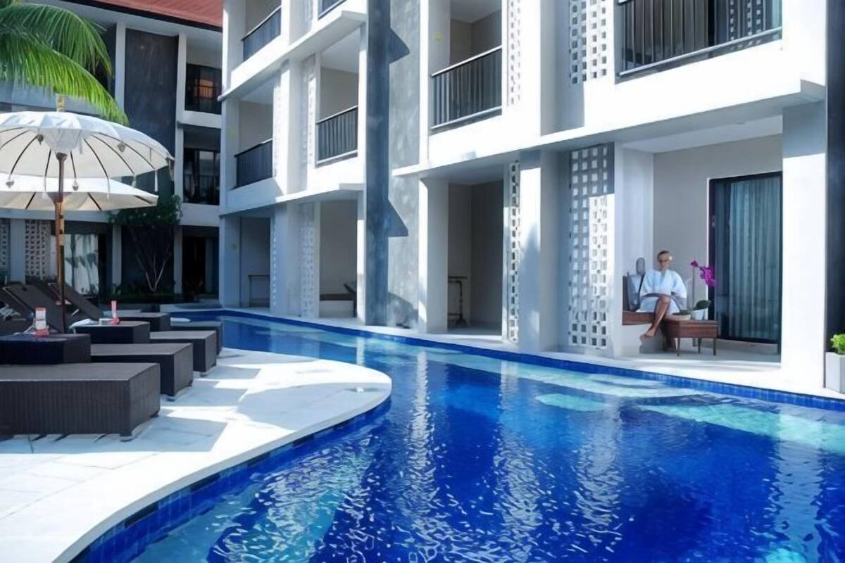 A modern hotel with a swimming pool, outdoor seating, and a two-story building.