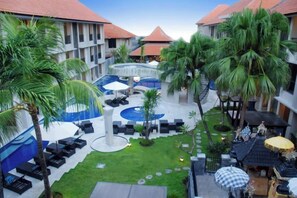 A courtyard with a pool, lounge chairs, palm trees, and a small garden area. - Grand Barong Resort (Bali)