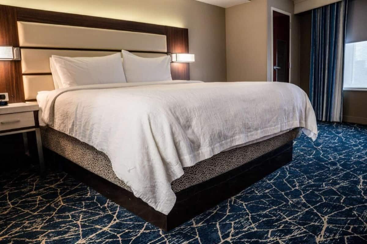 A hotel room with a large bed, a nightstand, a lamp, and a window with curtains.