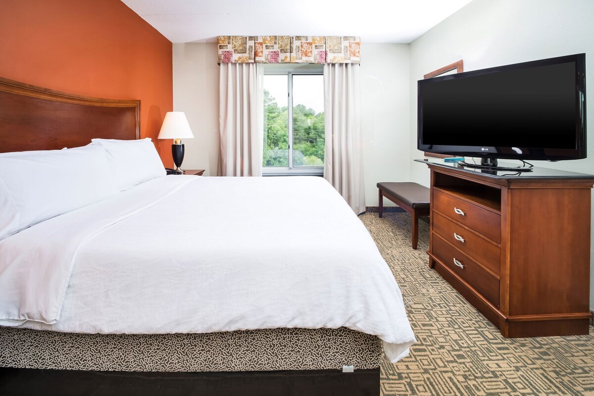 A hotel room with a bed, a television, a desk, and a window with curtains.