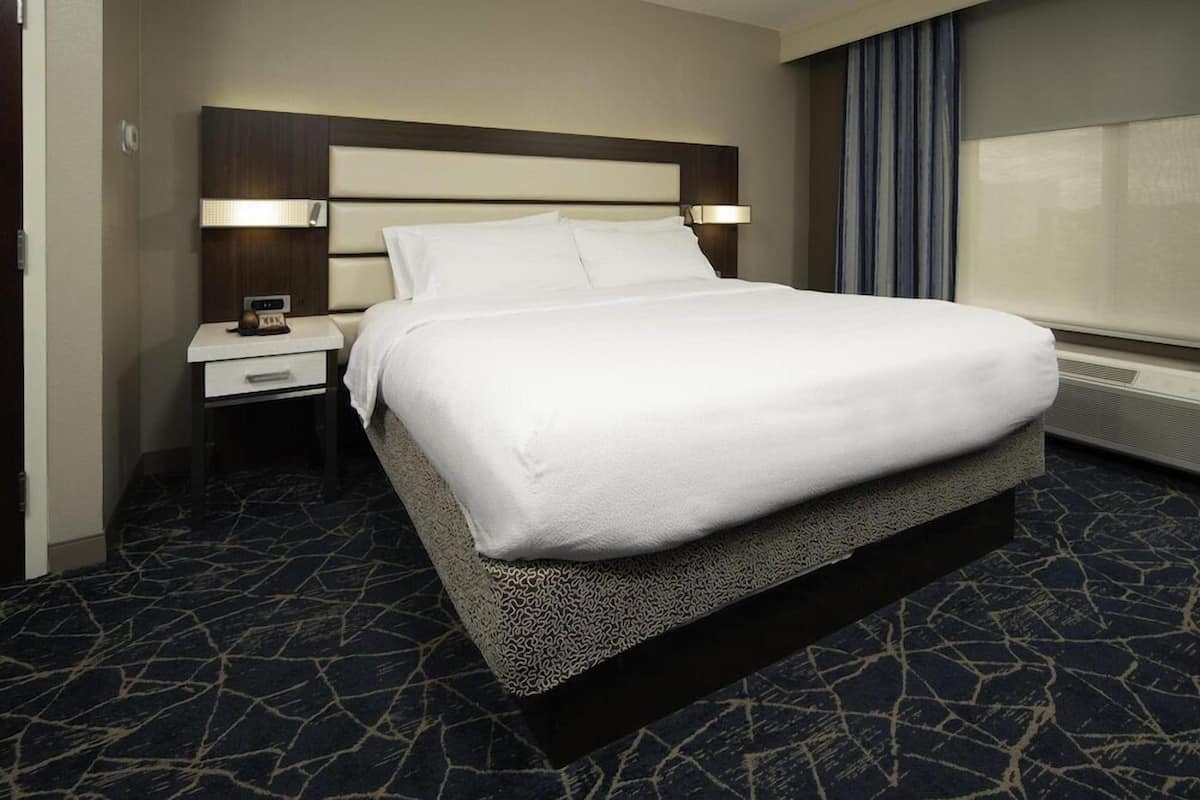 A hotel room with a bed, a nightstand, a lamp, and a window with curtains.