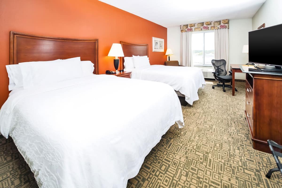 A hotel room with two beds, a desk, a television, and a window with curtains.