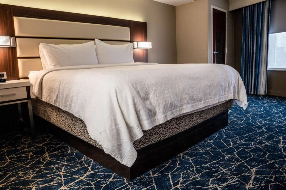 A hotel room with a large bed, a nightstand, a lamp, and a window with curtains.