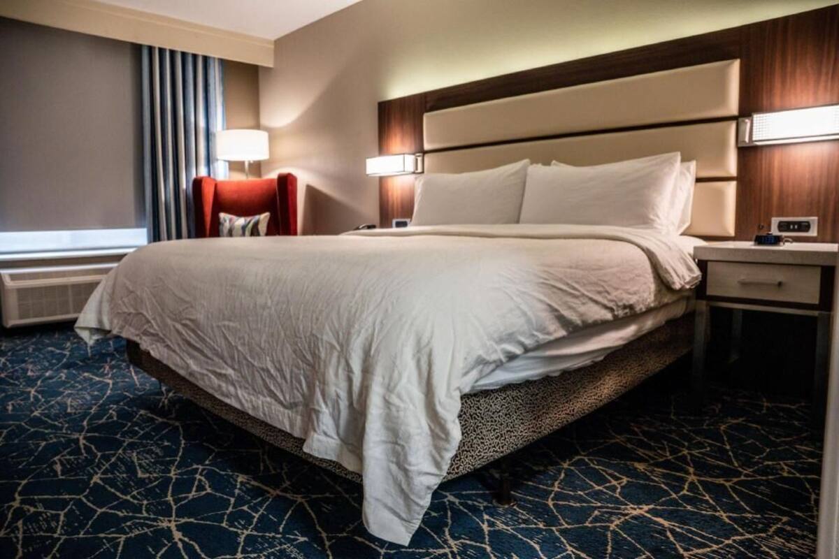 A hotel room with a large bed, two bedside tables, a red chair, and a window with curtains.