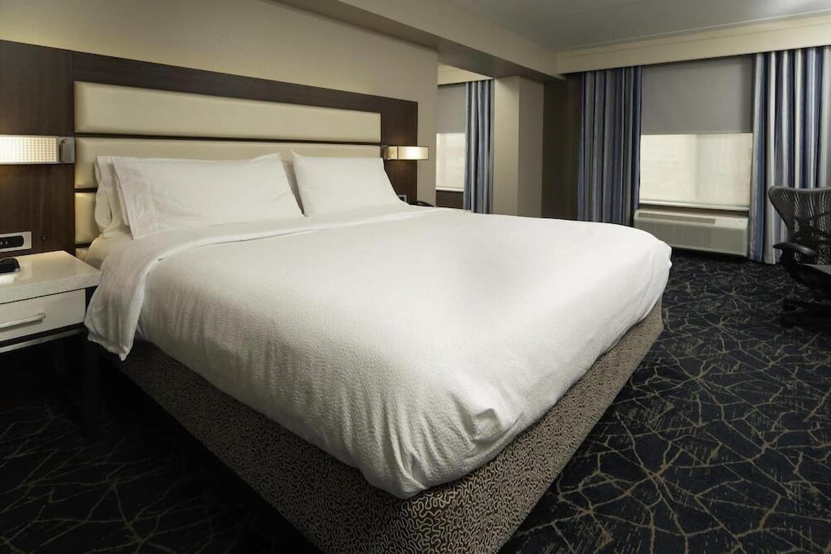 A hotel room with a large bed, a nightstand, a chair, and a window with curtains.