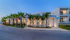 A modern hotel with a curved facade, palm trees, and a visible sign for Delfina Art. - Delfina Boutique (Apokoronas)