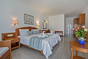 A hotel room with a bed, bedside tables, a desk, a chair, a vase with flowers, a mirror, and a wall with a framed picture. - Delfina Boutique (Apokoronas)