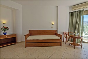 Una habitación con una cama de madera, una pequeña mesa con dos sillas, un jarrón con flores y una ventana con cortinas.