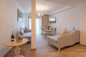 A modern living room with a sofa, a dining table with chairs, a small round table with a bottle and glasses, and a television on the wall. - Delfina Boutique (Apokoronas)