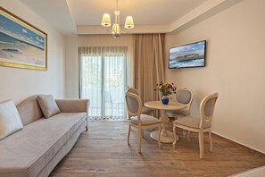 A room with a sofa, dining table with chairs, a chandelier, and two framed pictures on the walls. - Delfina Boutique (Apokoronas)