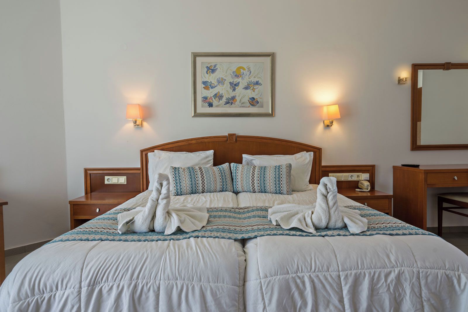 A double bed with a wooden headboard, two bedside tables, patterned pillows, and a framed artwork above.