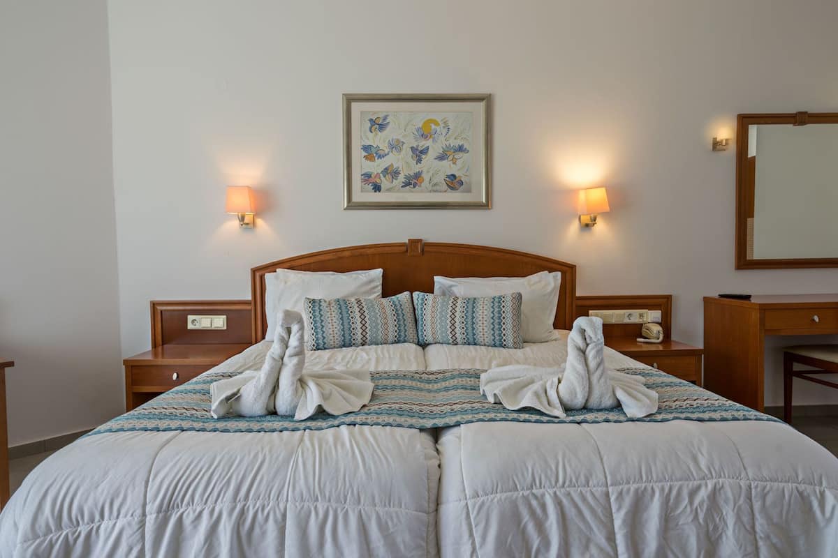 A double bed with a wooden headboard, two bedside tables, patterned pillows, and a framed artwork on the wall.