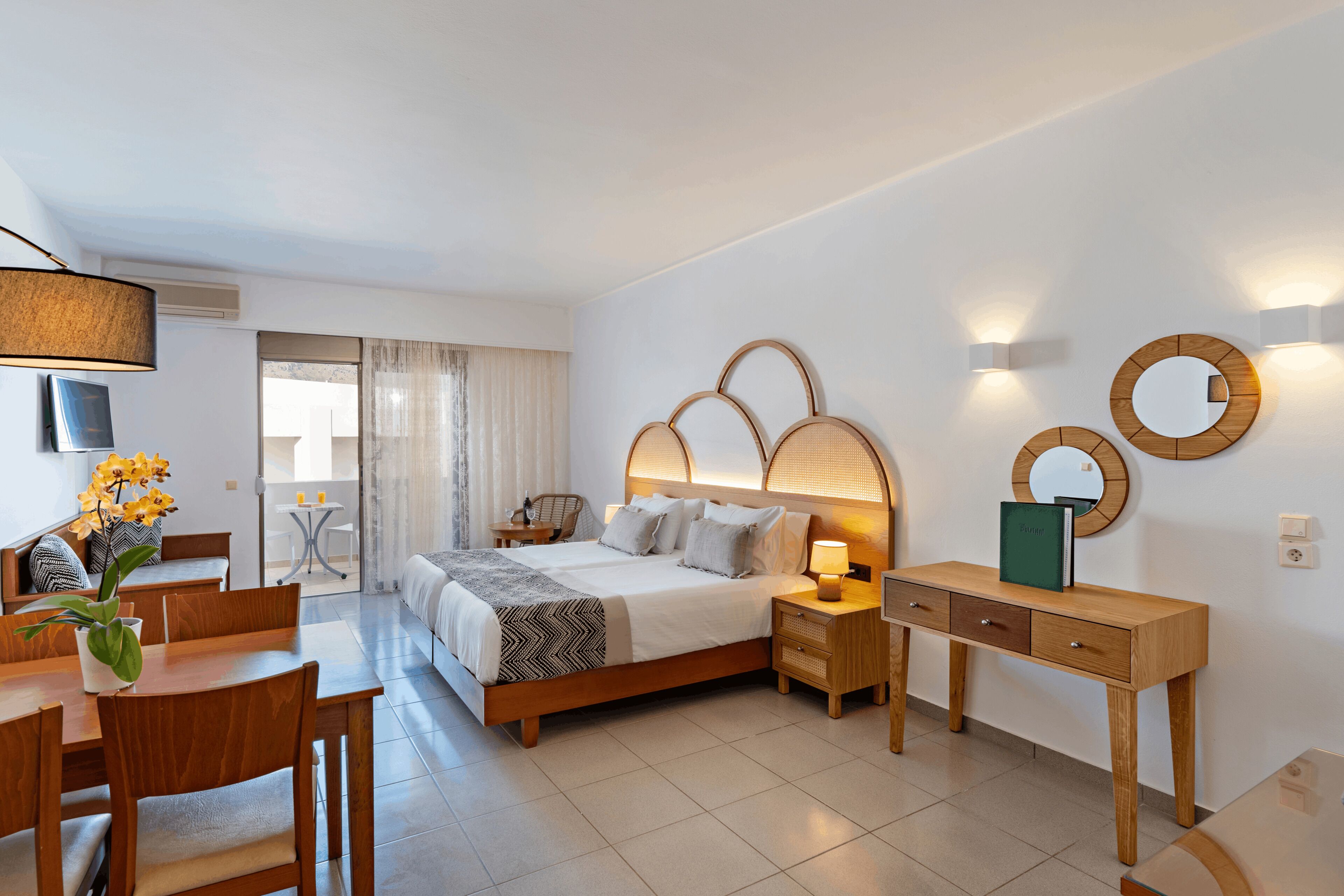 Quarto de hotel moderno com cama, mesas de cabeceira, escrivaninha e área de refeições.