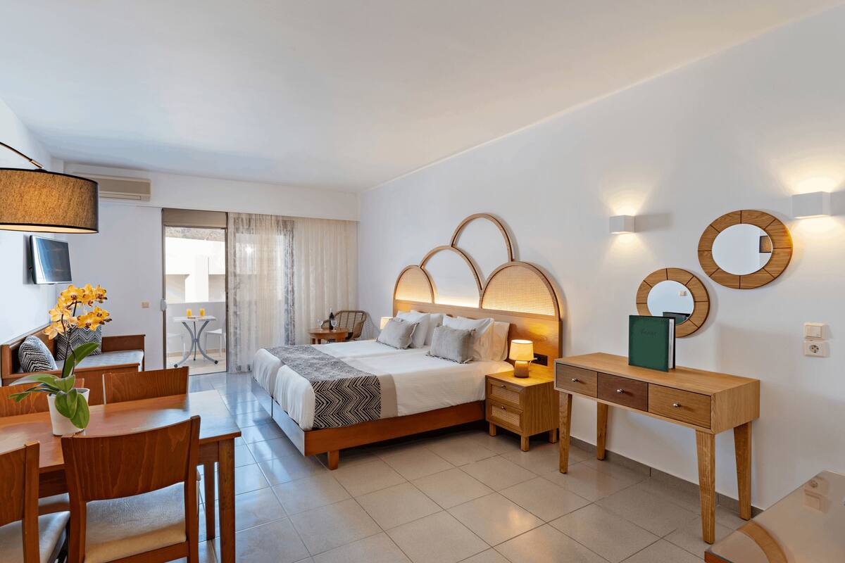 A modern hotel room with a bed, bedside tables, a desk, and a dining area.
