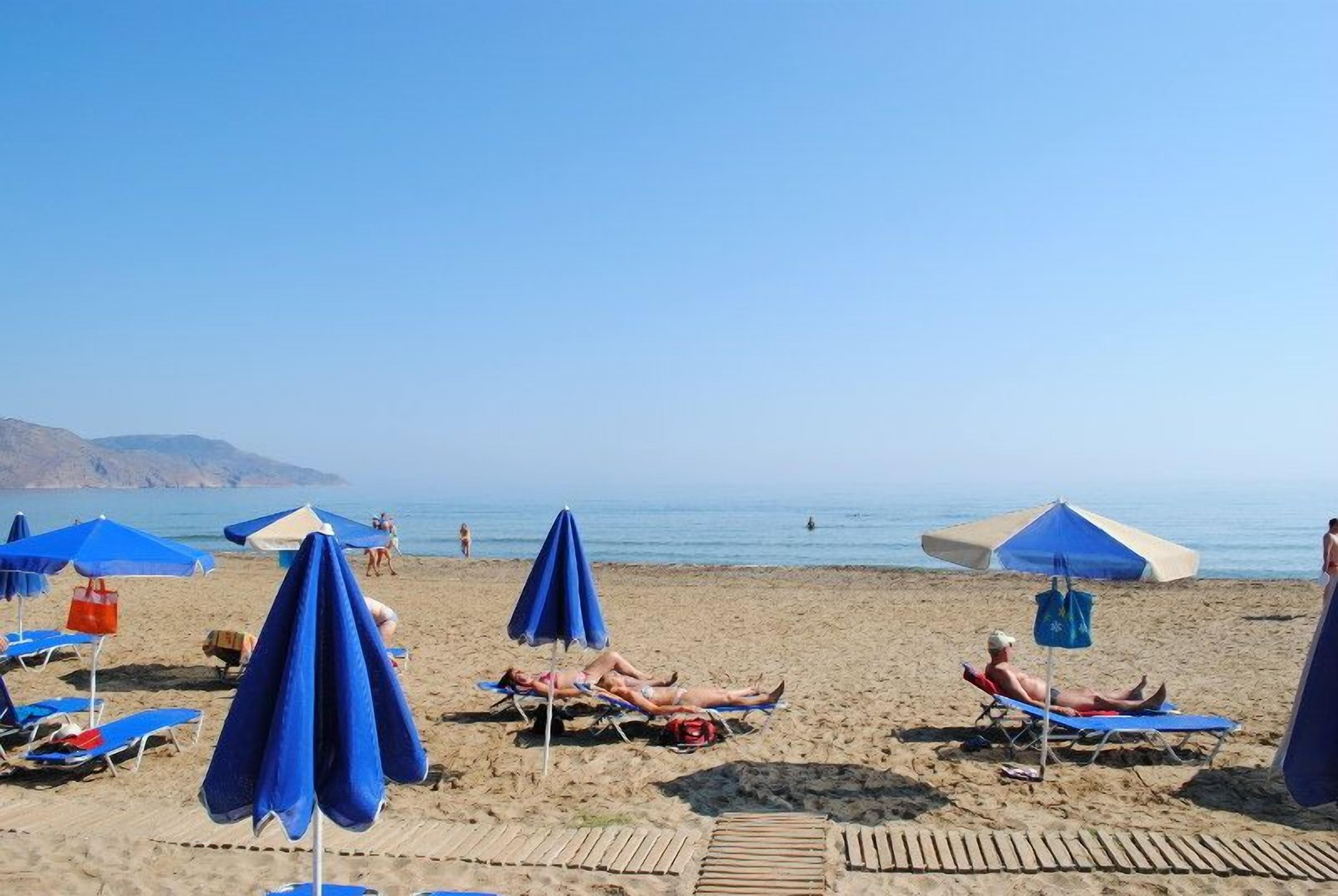 A beach with multiple blue umbrellas and lounge chairs.