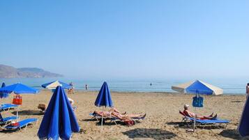 A beach with multiple blue umbrellas and lounge chairs.