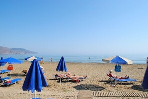 A beach with multiple blue umbrellas and lounge chairs. - Delfina Boutique (Apokoronas)