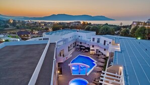 A rooftop pool area with multiple pools and lounge chairs, surrounded by a white building with balconies. - Delfina Boutique (Apokoronas)