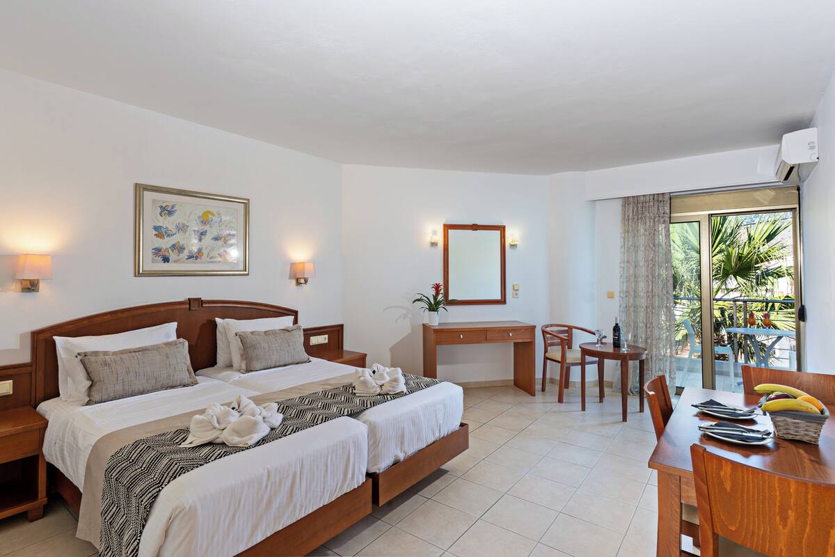 A hotel room with a bed, desk, chair, dining table, and a balcony with plants.