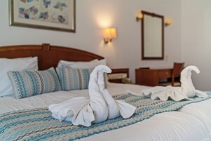 Una habitación de hotel con una cama bien tendida, cabecera de madera, mesita de noche y lámpara de pared.
