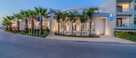 A modern hotel with a flat facade, palm trees, and a sign reading 'DEFINA ART'.