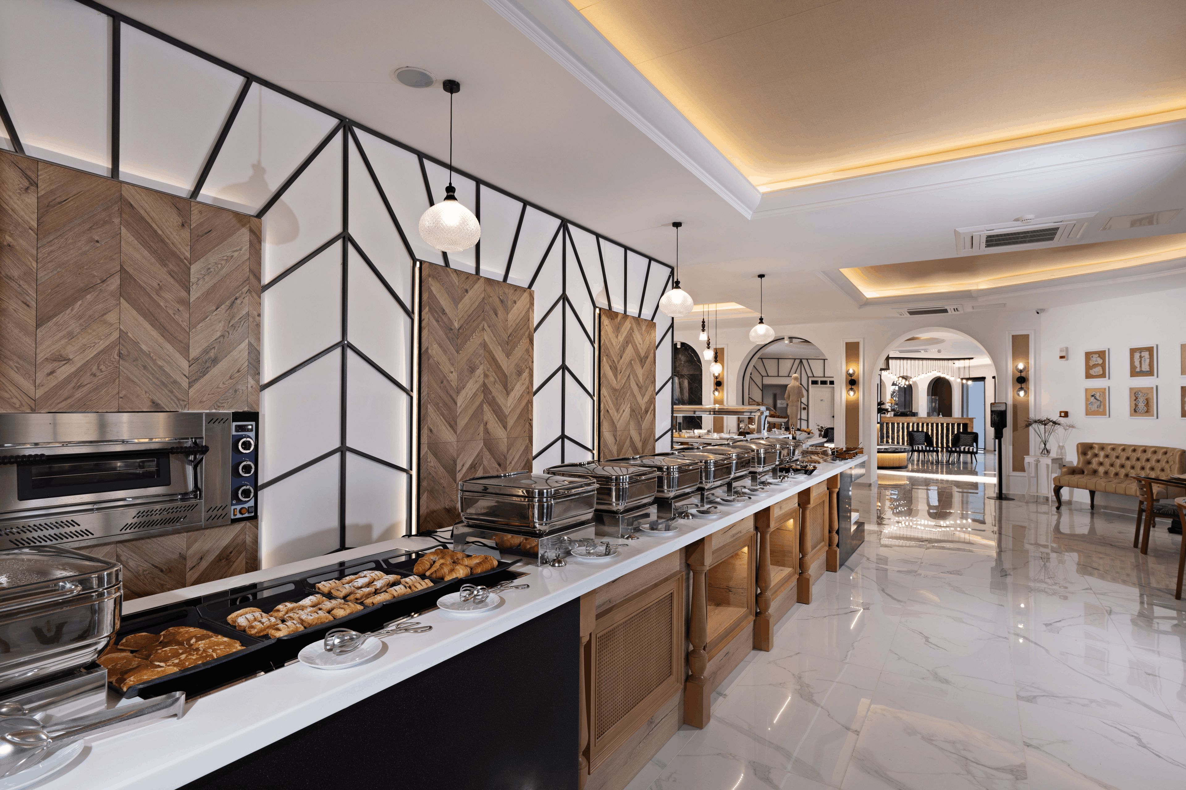 A modern hotel kitchen with a buffet setup, a built-in oven, and a seating area with a sofa and table.