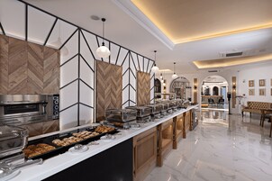 A modern hotel kitchen with a buffet setup, a built-in oven, and a seating area with a sofa and table.
