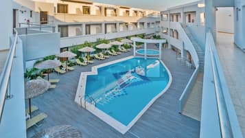 A modern hotel with a central swimming pool, sun loungers, and a covered seating area.