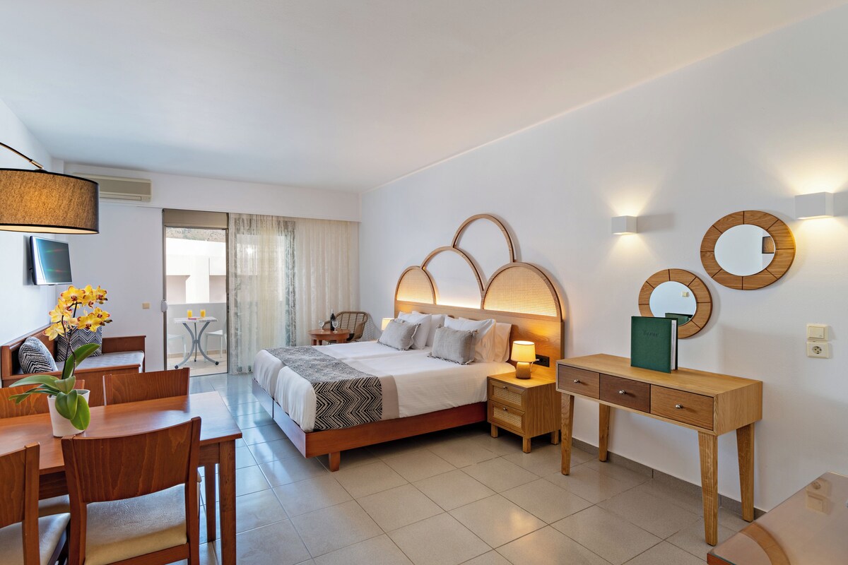 A modern hotel room with a bed, bedside tables, a desk, and a dining area.