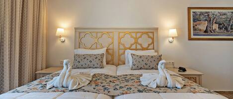 Une chambre d’hôtel avec un grand lit, deux tables de chevet, une tête de lit ornée d’un panneau décoratif, des lampes fixées au mur et un tableau accroché au mur.