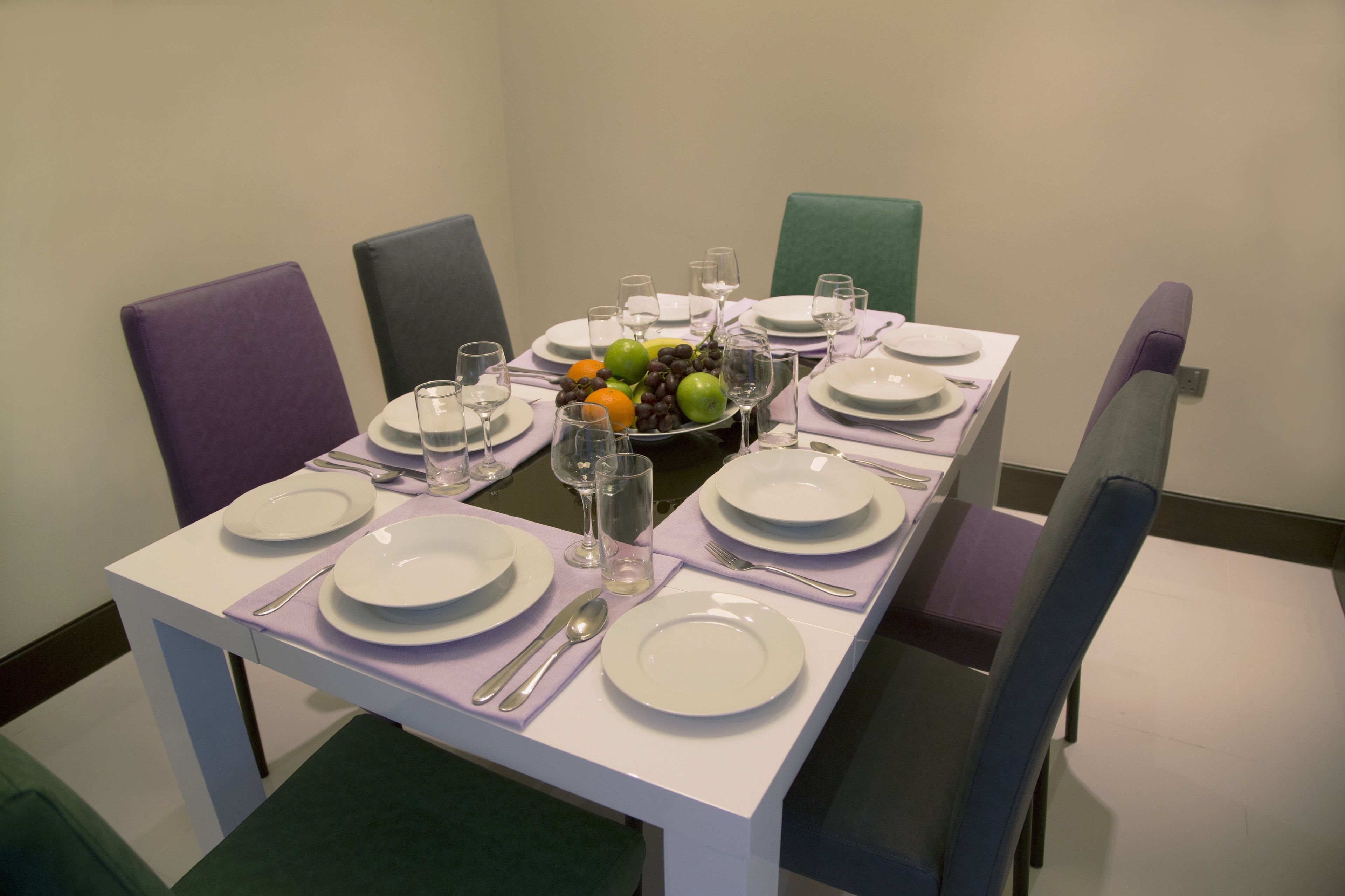 A dining table set with plates, cutlery, glasses, and a fruit bowl.