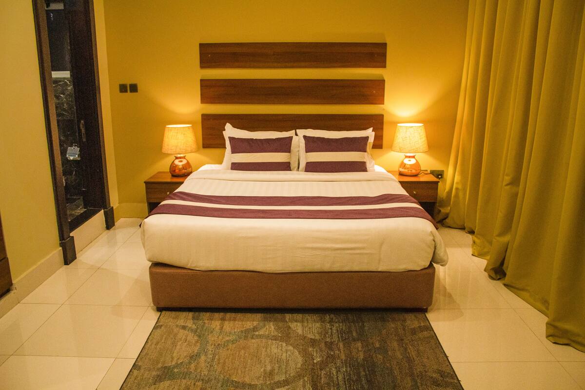 A hotel room with a large bed, two bedside lamps, and a headboard with horizontal wooden panels.