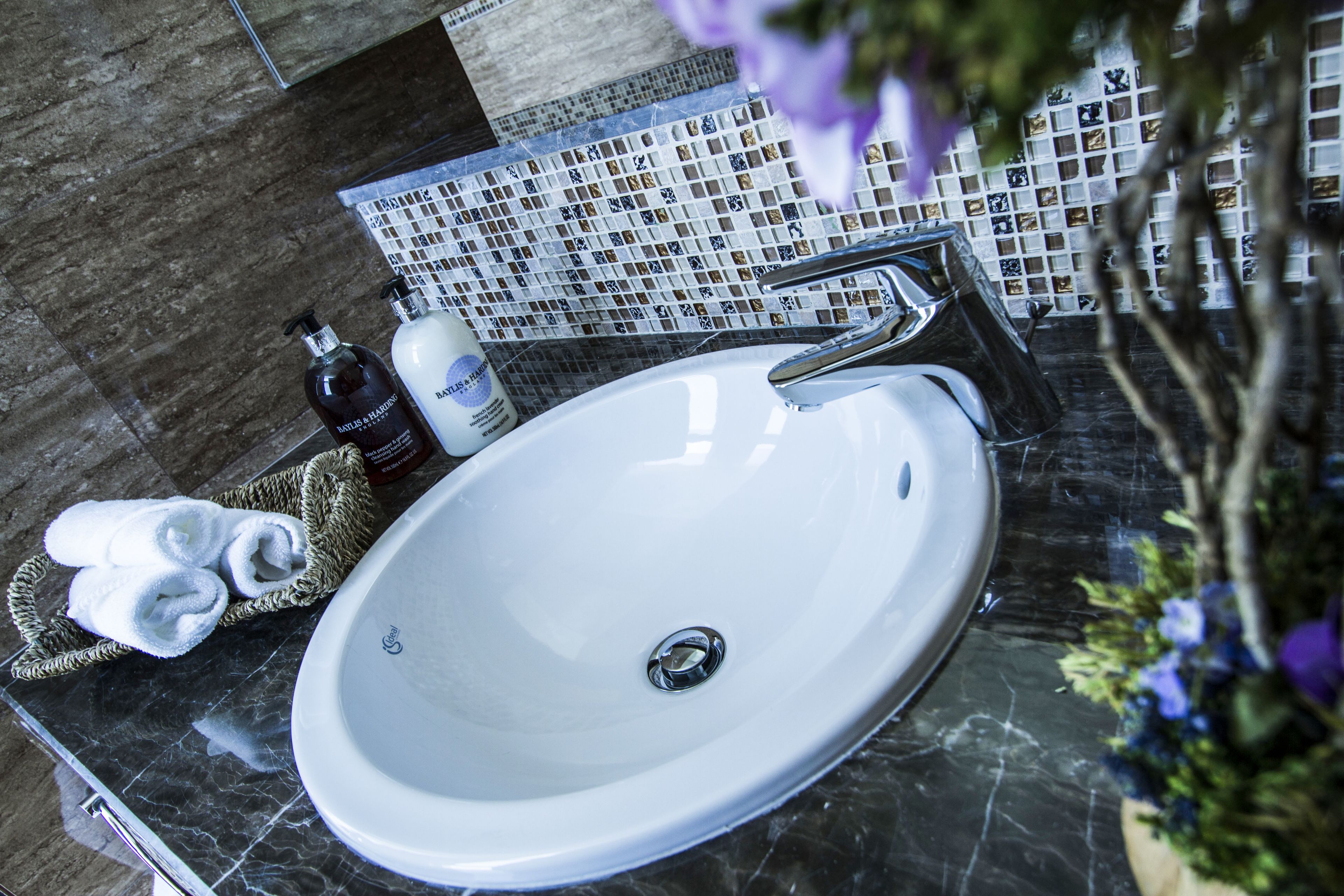 A bathroom with a white sink, a chrome faucet, and a tiled backsplash. There are towels and toiletries on the counter.