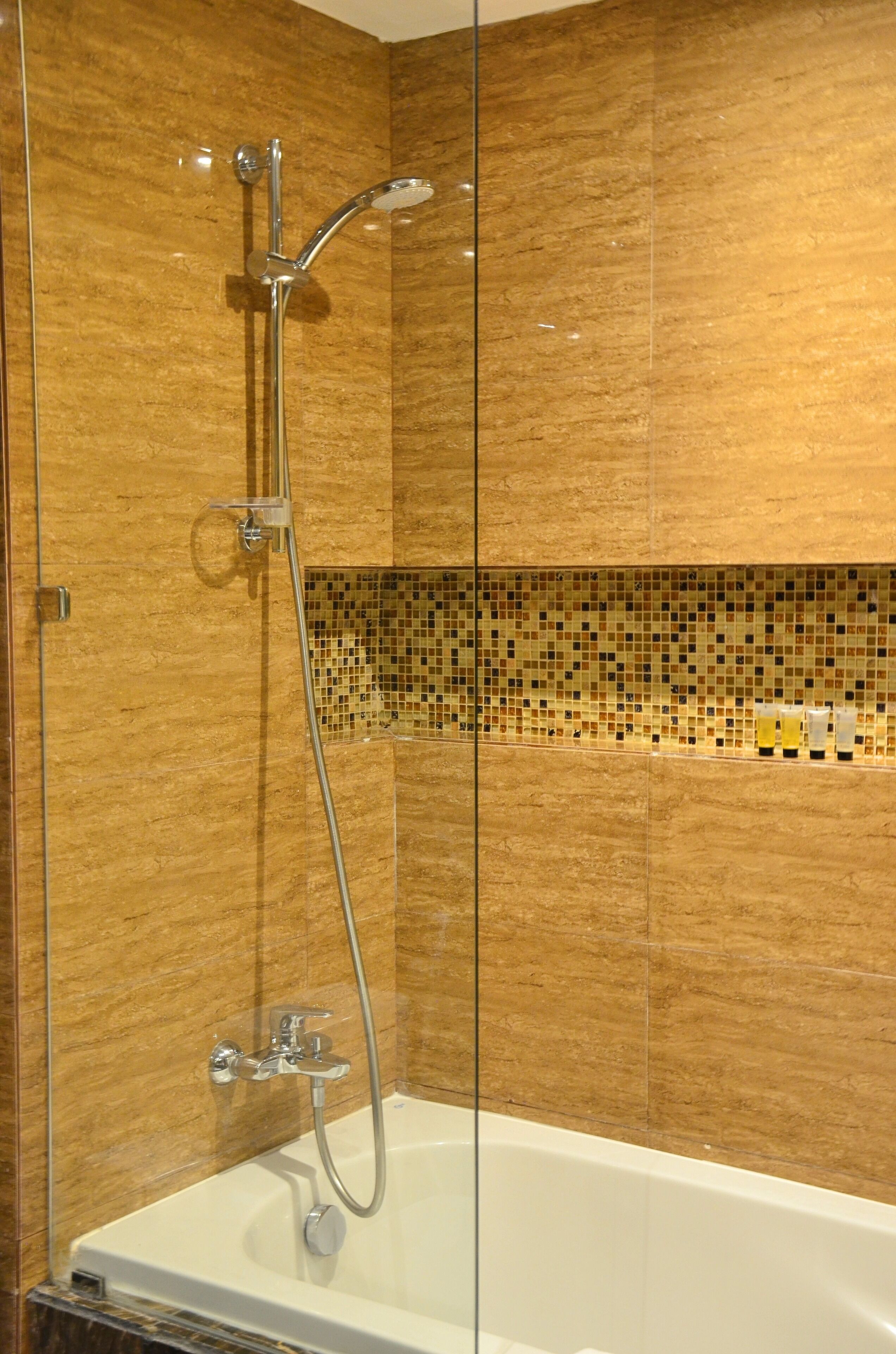 A modern bathroom with a glass-enclosed shower, a white bathtub, and mosaic tile walls.