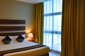 Una habitación de hotel con cama, mesita de noche, lámpara y ventana con cortinas.