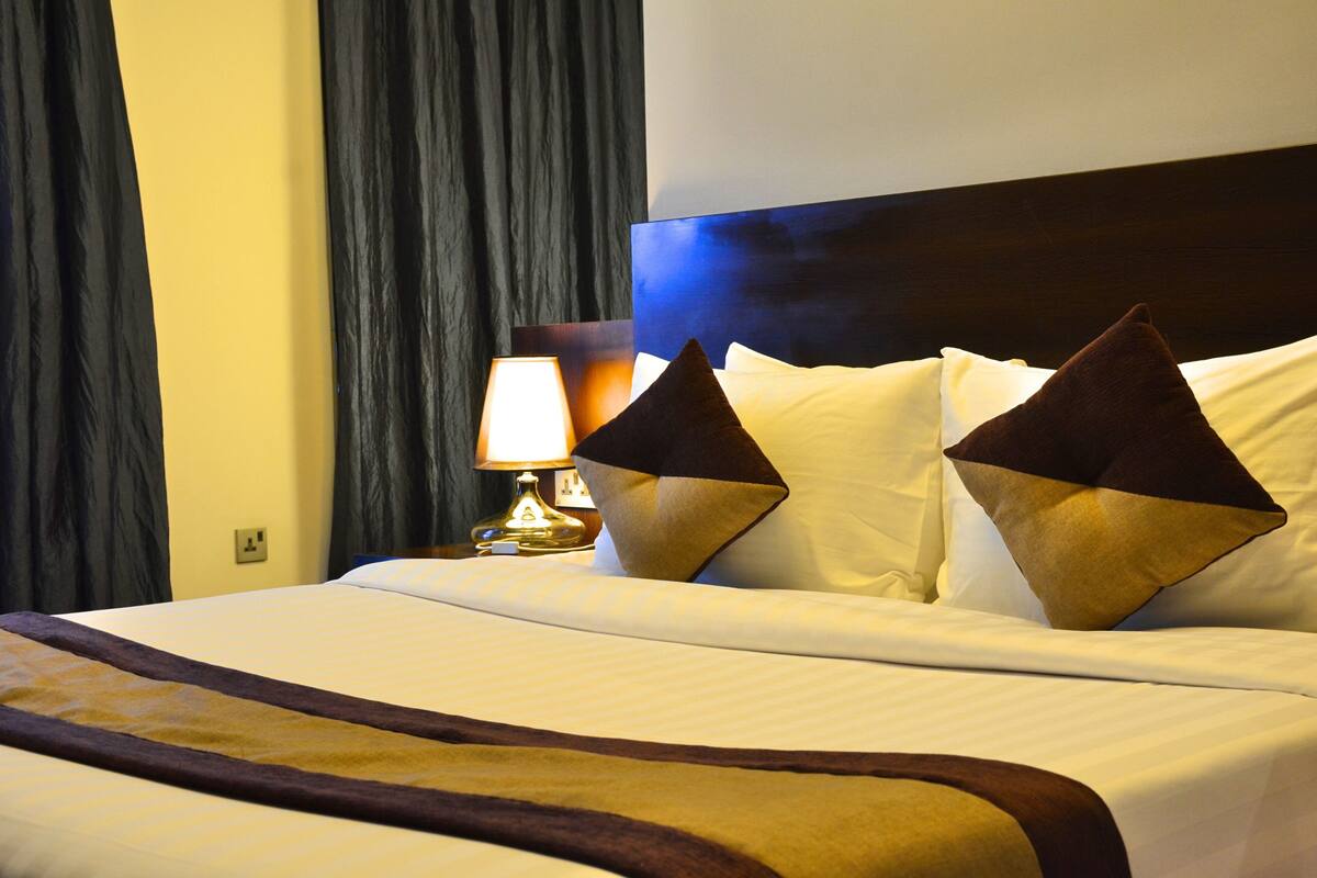 A neatly made bed with a headboard, two pillows, and a bedside lamp.