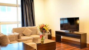 Una sala de estar moderna con un sofá beige, una mesa de centro, un televisor sobre un mueble bajo y un jarrón con flores.