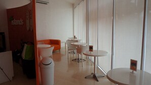 A modern, well-lit indoor space with a curved wall, a seating area with an orange couch, multiple white tables, and a trash bin. - Islands Stay Hotels Uptown (Cebu)