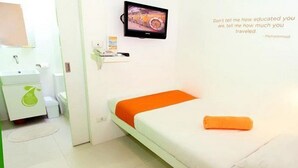 A small, bright room with a bed, a TV, and a small table with a chair. - Islands Stay Hotels Uptown (Cebu)