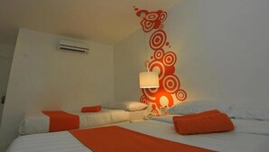 A hotel room with a bed, orange pillows, a wall-mounted lamp, and an air conditioning unit. - Islands Stay Hotels Uptown (Cebu)