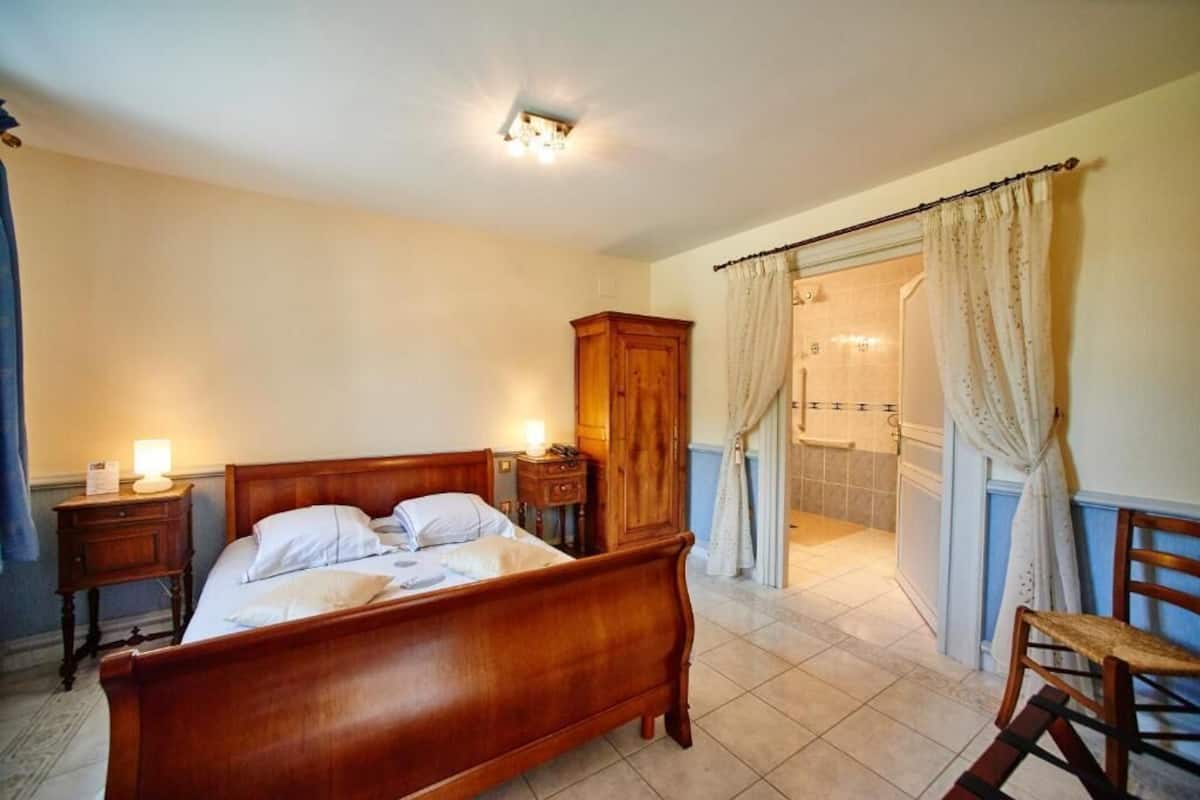 Quarto com cama de madeira, mesas de cabeceira, um criado-mudo, guarda-roupa de madeira e um banheiro visível através de uma cortina.